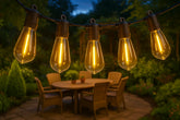 String of illuminated light bulbs hanging above an outdoor dining table with a blurred background